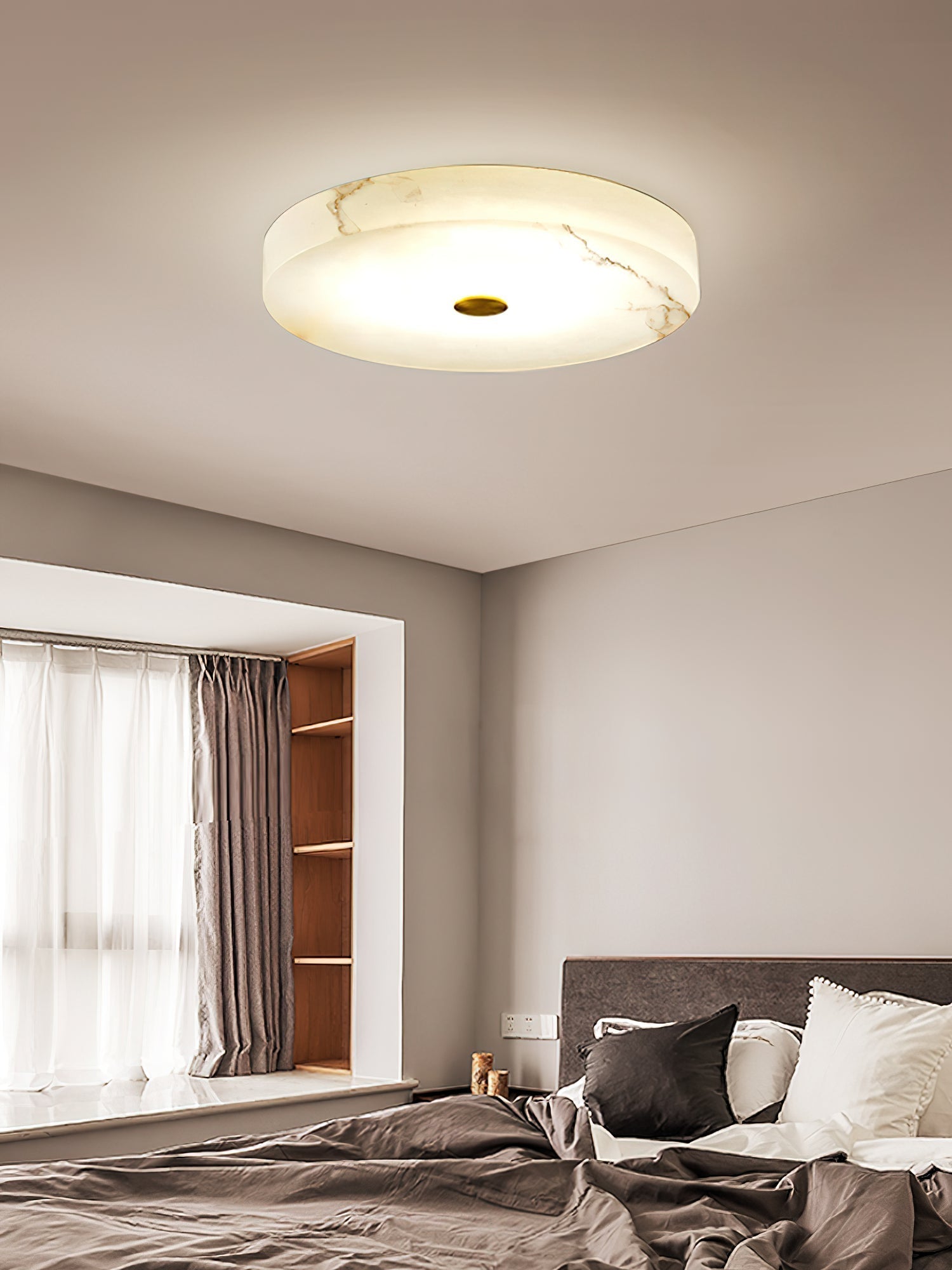 Clérachic alabaster flush mount ceiling light above a bedroom bay window, its stone veining rising warm through the lit surface.