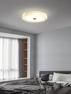 Clérachic alabaster ceiling light in a grey bedroom, veining showing warm through the stone above a bay window seat.