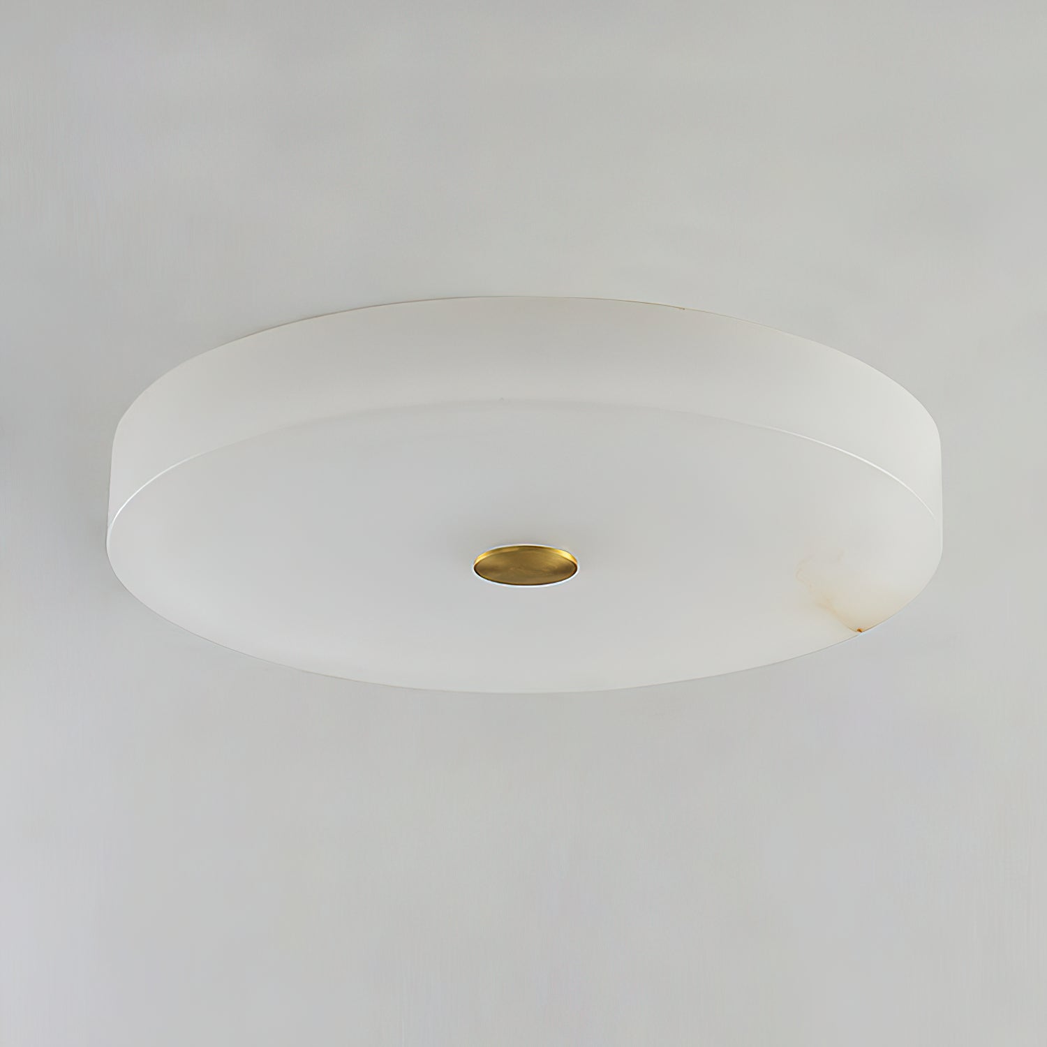 Unlit studio view of the Clérachic drum flush mount ceiling light, cool white stone with a polished brass disc at its centre.