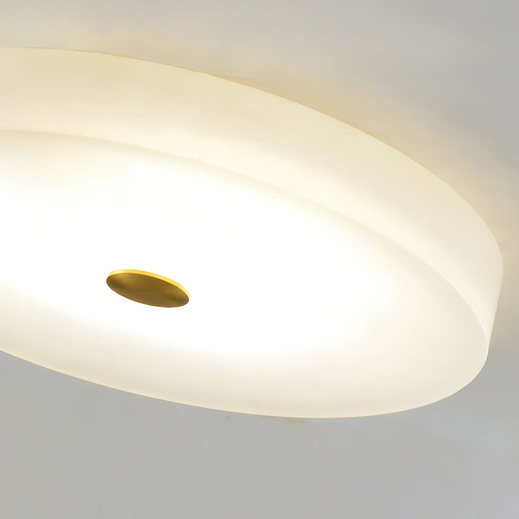 Close crop of the Clérachic ceiling light's lit underside, alabaster glowing evenly around the brushed brass centre cap.
