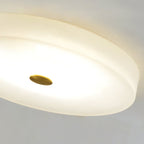 Close crop of the Clérachic ceiling light's lit underside, alabaster glowing evenly around the brushed brass centre cap.