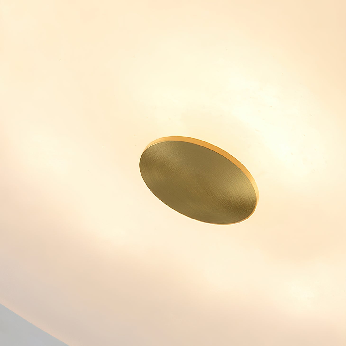 Macro of the brushed brass centre cap on the Clérachic alabaster ceiling light, set into the warm glowing stone underside.