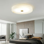 Clérachic flush mount ceiling light in a pale bedroom with cornice mouldings, glowing softly above the bed and leaning artwork.