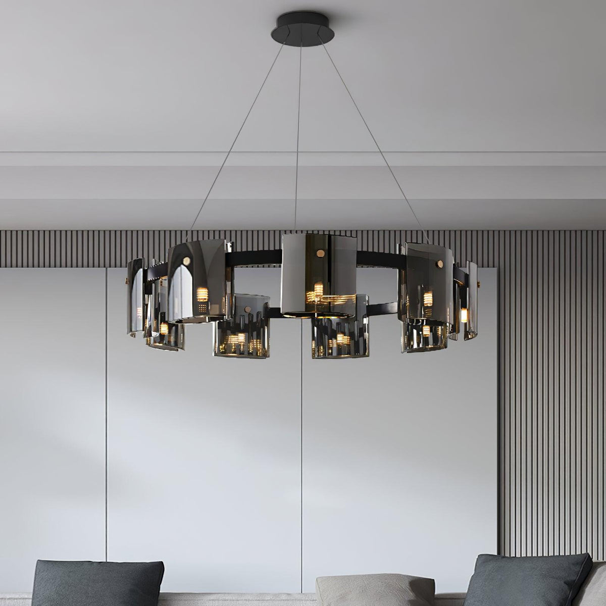 Close, lit view of a black-frame Clérachic chandelier with smoked glass shades over a grey panelled wall and dark sofa cushions.