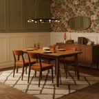 A black-frame ring chandelier from Clérachic over a walnut dining table, with orange chairs, a green panelled wall and floral wallpaper.