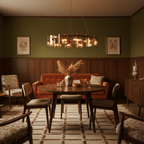 Warm-lit Clérachic chandelier over a round dining table in a room with olive walls, wood panelling and an orange sofa.
