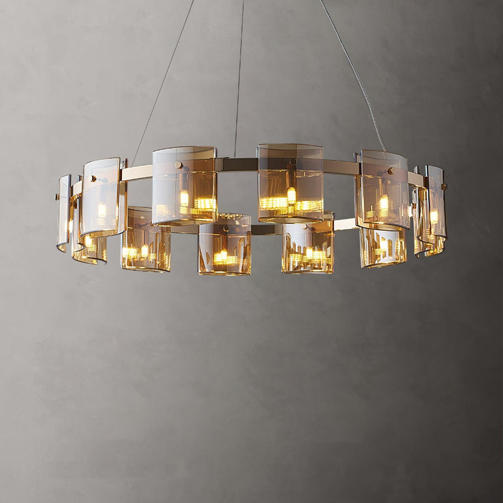 Lit gold-frame ring chandelier from Clérachic with amber glass shades of different heights, against a mid-grey wall.