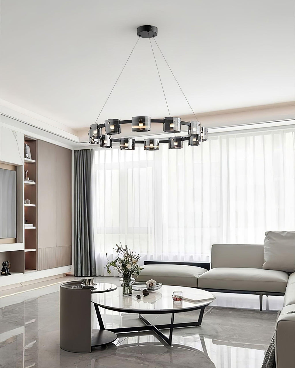 Distant view of a black ring chandelier from Clérachic in a bright living room with a glass coffee table, a pale sofa and sheer curtains.
