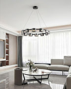 Distant view of a black ring chandelier from Clérachic in a bright living room with a glass coffee table, a pale sofa and sheer curtains.