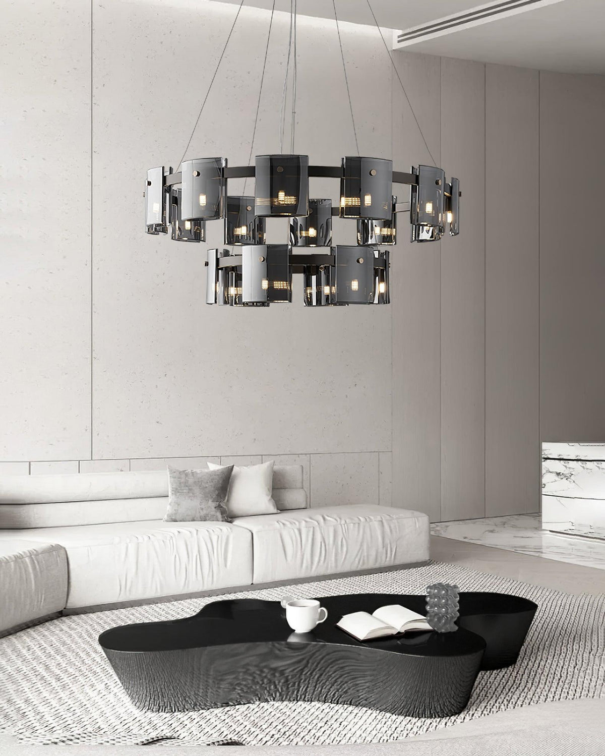 Two-tier black chandelier from Clérachic with smoked glass shades hanging above a black coffee table in a white lounge.
