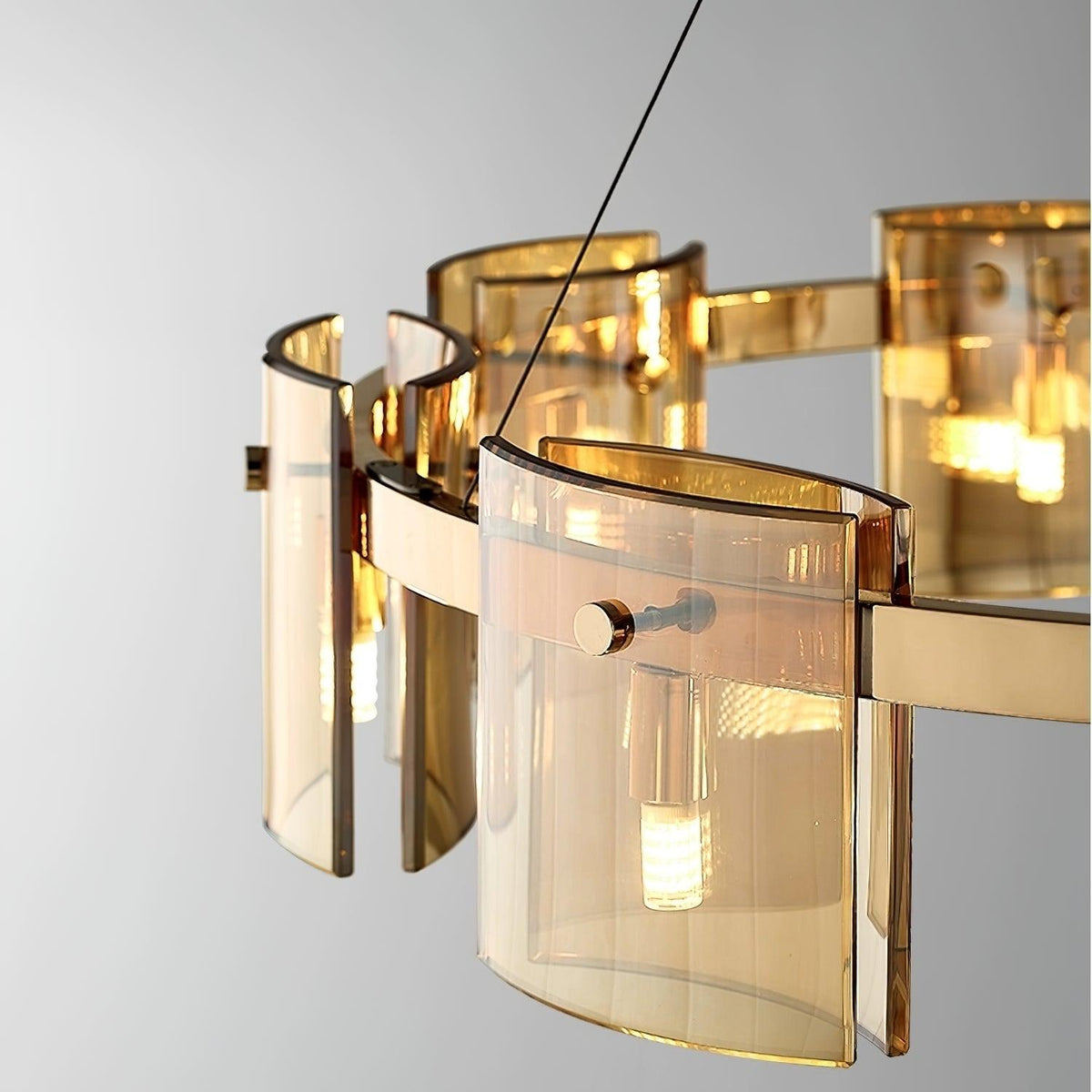 Close view of curved amber glass panels on the gold band of this Clérachic chandelier, with a small bulb visible inside.