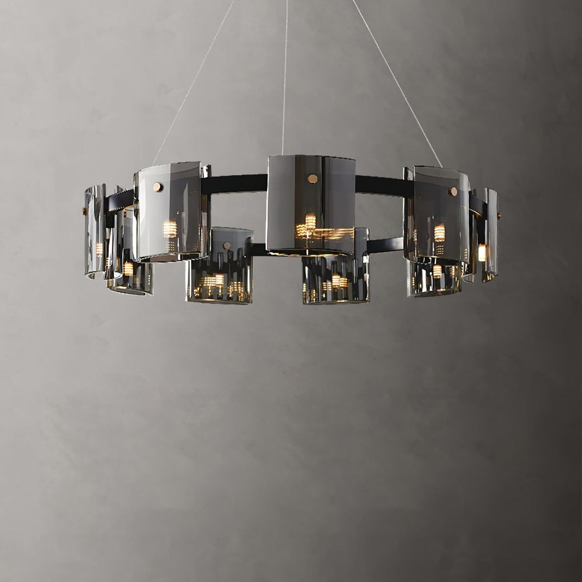 Wide black ring chandelier from Clérachic with smoked glass shades hung in staggered heights on thin cables against a grey wall.
