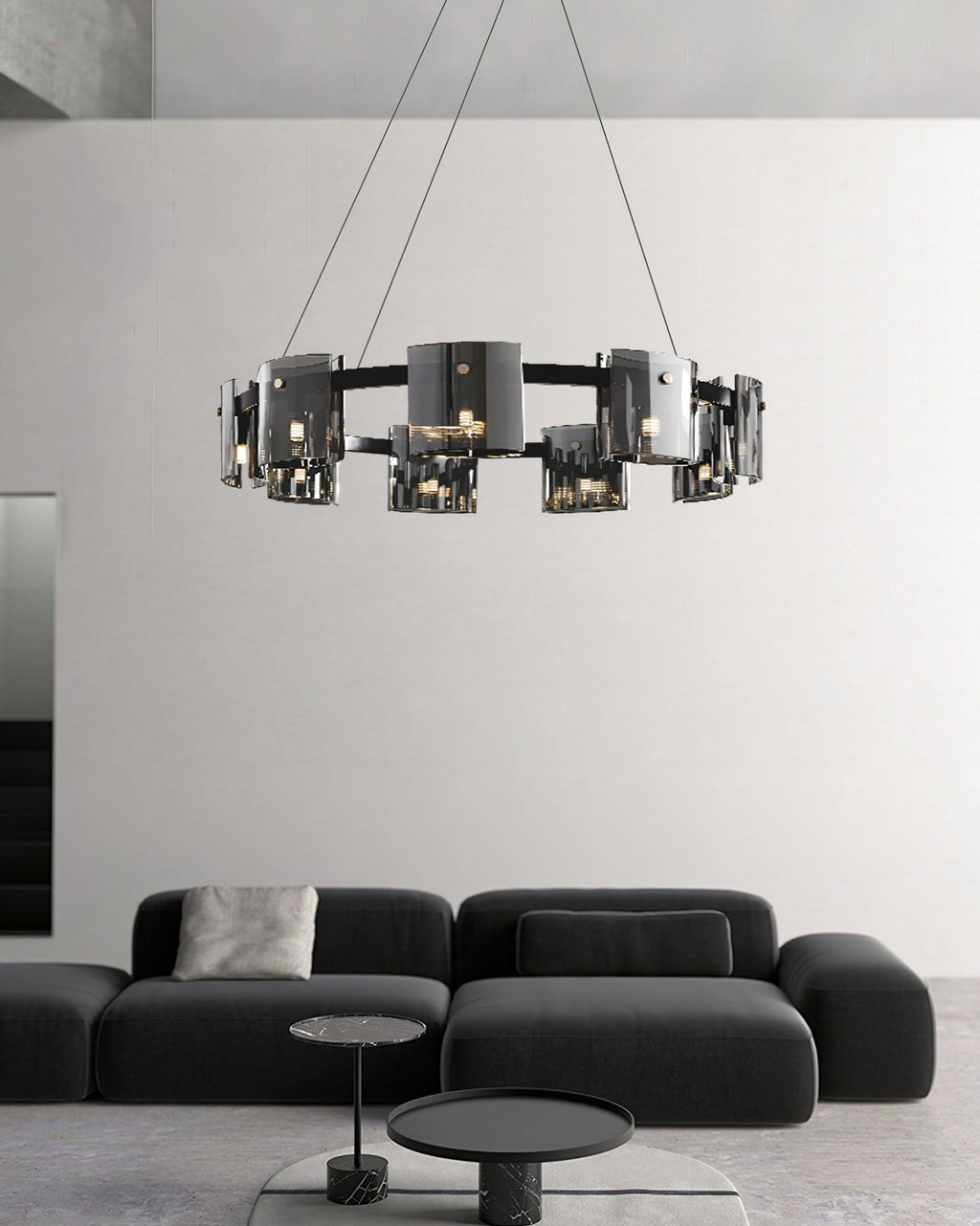Black ring chandelier from Clérachic with smoked glass shades above a low black sofa and two small round side tables.