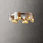 Gold-frame ring chandelier from Clérachic with amber glass shades, lit warm and hung on thin cables against a grey wall.