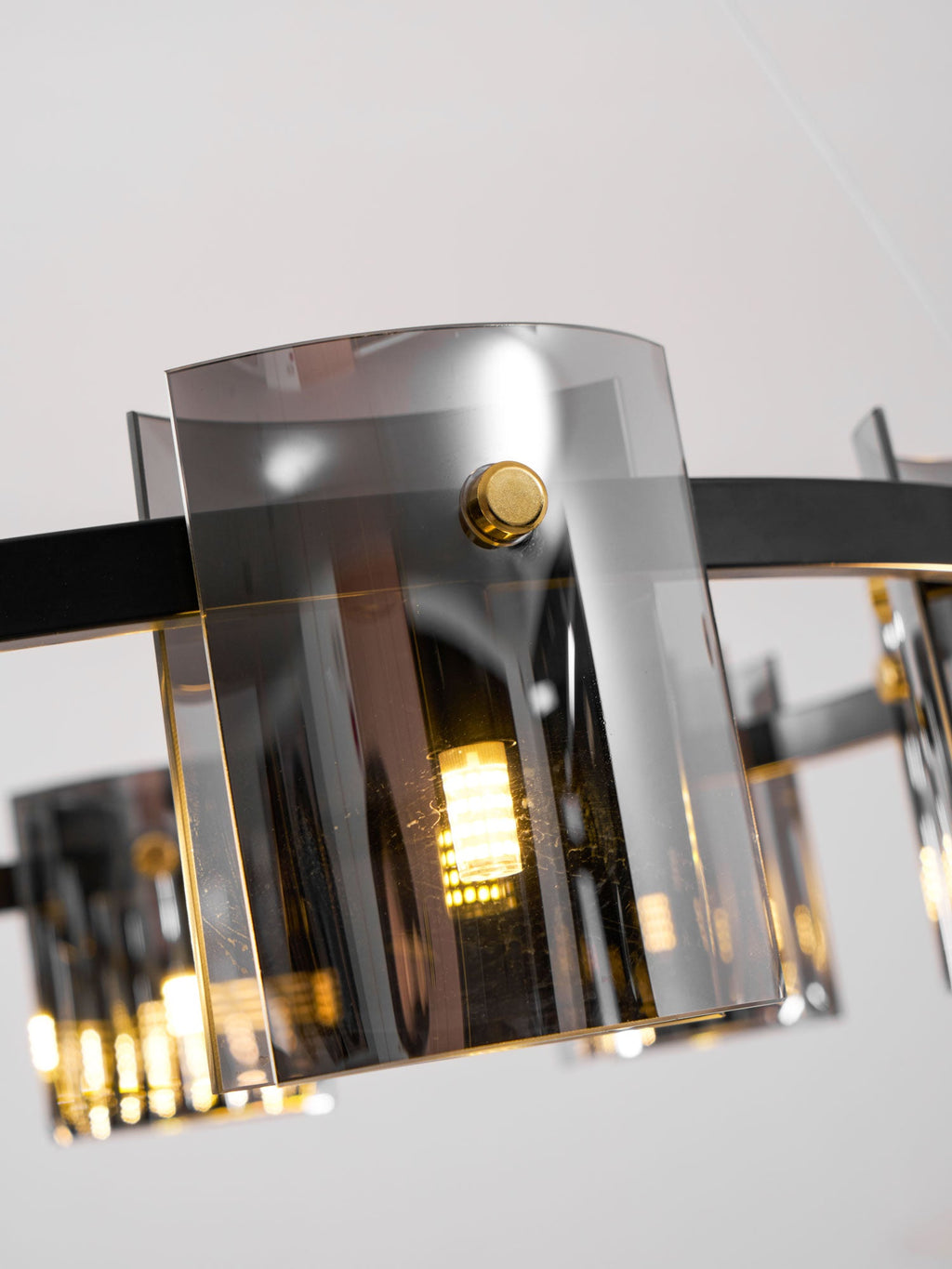 Close view of a smoked glass shade on this Clérachic chandelier, with a brass-coloured knob and a bulb glowing inside.