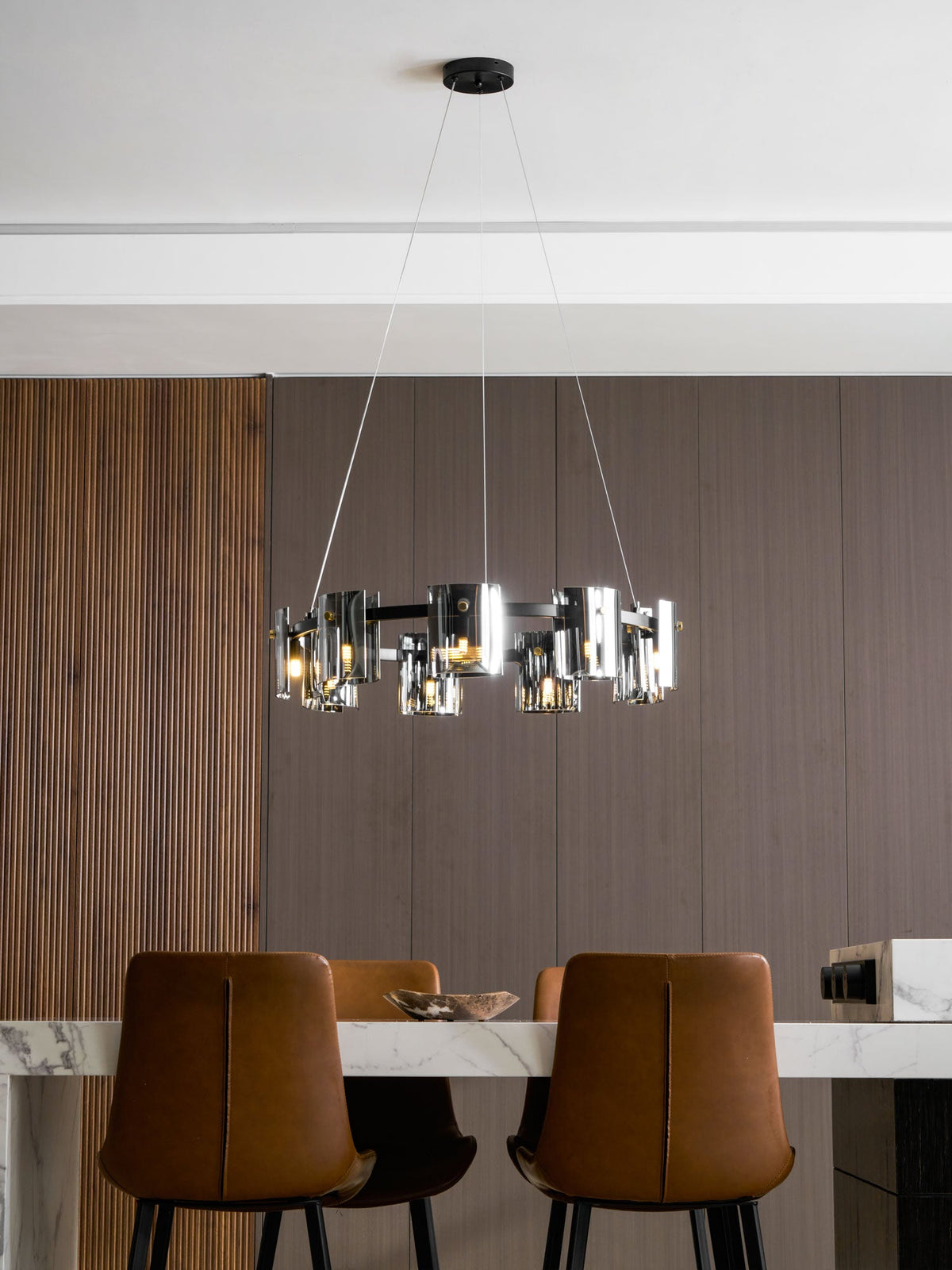 Lit black-frame chandelier from Clérachic with smoked glass shades above a marble table and tan leather chairs.