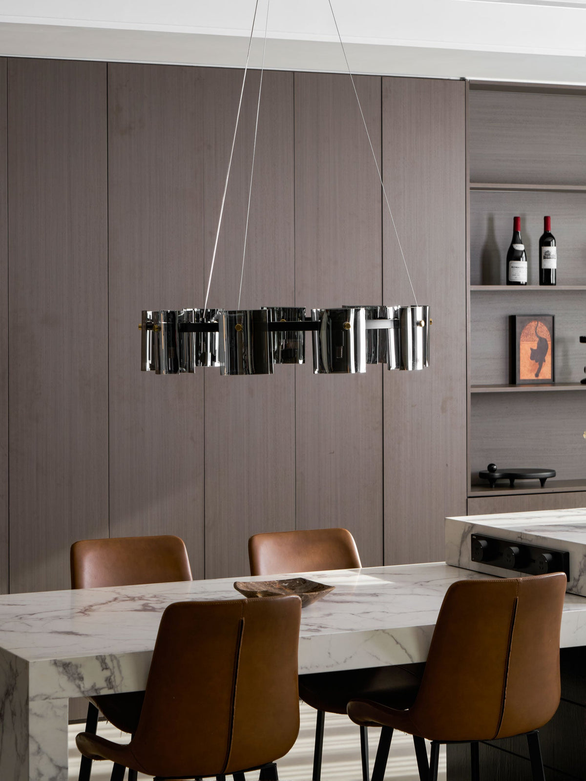 Black ring chandelier from Clérachic seen edge-on in a dining room, with a marble table, wine bottles on shelves and leather chairs.