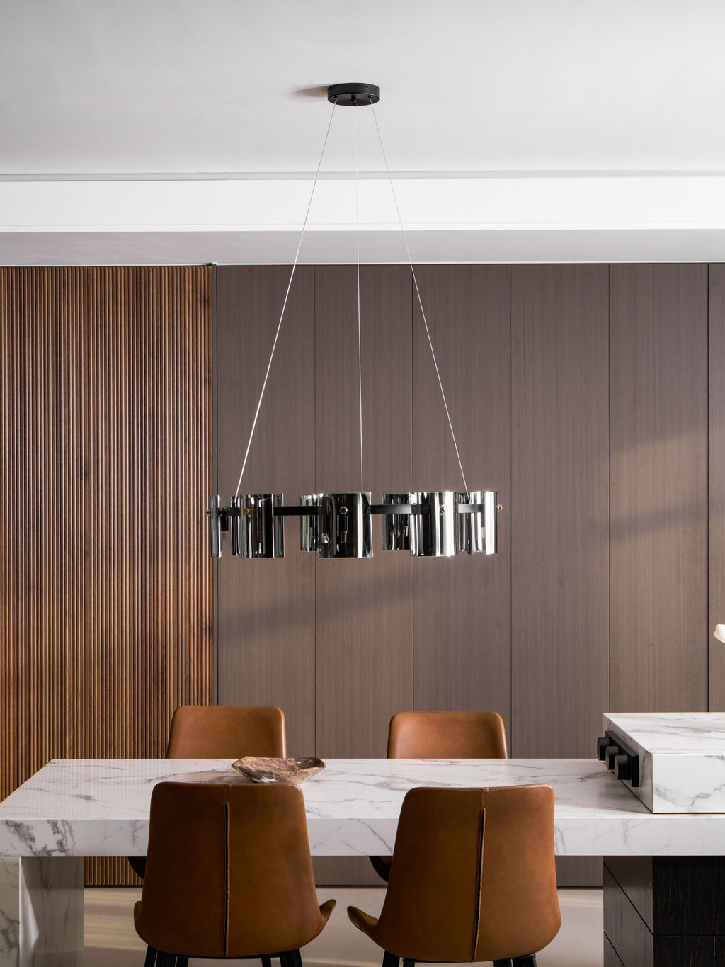 Black ring chandelier from Clérachic with smoked glass shades above a dining area, seen from a distance below a white ceiling.
