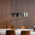 Smoked glass chandelier from Clérachic hung against a ribbed wood wall, with a marble table and leather chairs below.