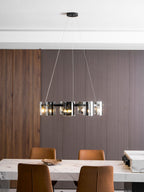 Lit black ring chandelier from Clérachic hung in a dining room with a ribbed wood panel wall and a marble table.