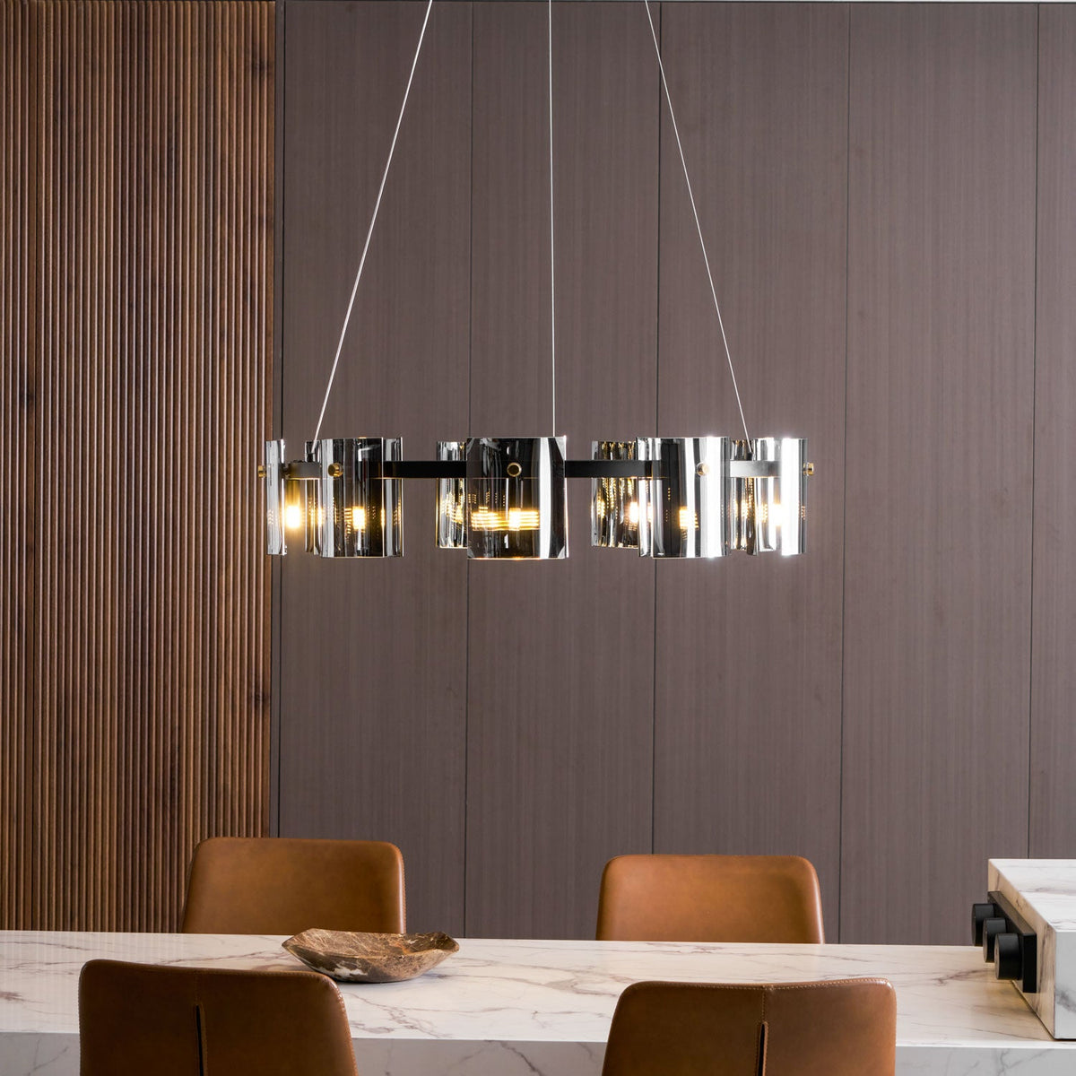 Chandelier from Clérachic with smoked glass shades lit, seen side-on in a dining room with wood panelling and tan chairs.