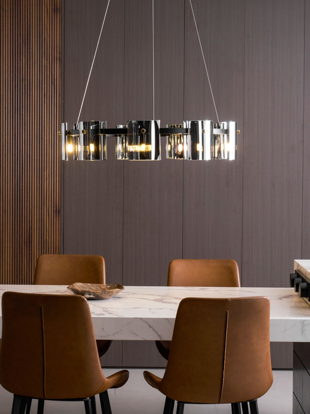 Smoked glass chandelier from Clérachic hanging side-on above a marble dining table and two leather chairs.