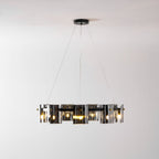Lit black ring chandelier from Clérachic with smoked glass shades hung low on three thin cables against a pale wall.