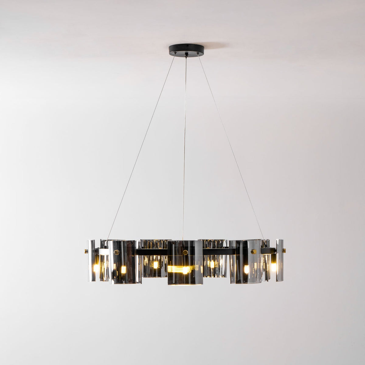 Lit black ring chandelier from Clérachic with smoked glass shades hung low on three thin cables against a pale wall.