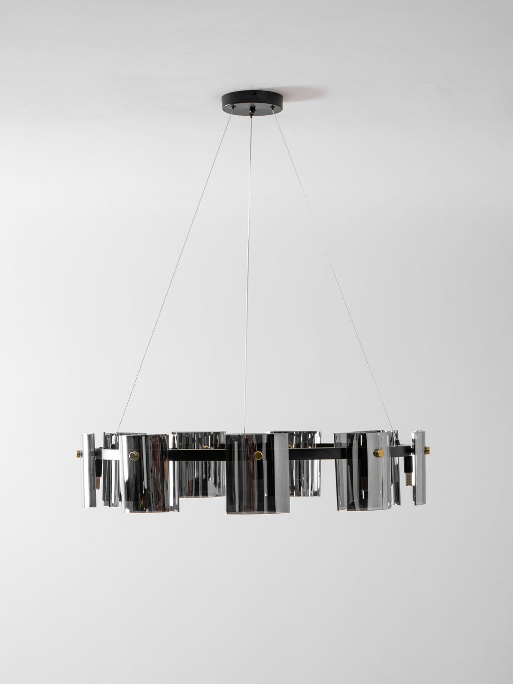Unlit black ring chandelier from Clérachic with smoked glass shades, seen edge-on on thin cables against a pale wall.