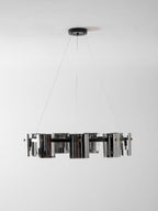 Unlit black ring chandelier from Clérachic with smoked glass shades, seen edge-on on thin cables against a pale wall.