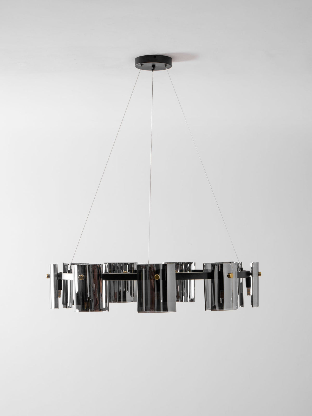 Unlit black ring chandelier from Clérachic with smoked glass shades, seen edge-on on thin cables against a pale wall.