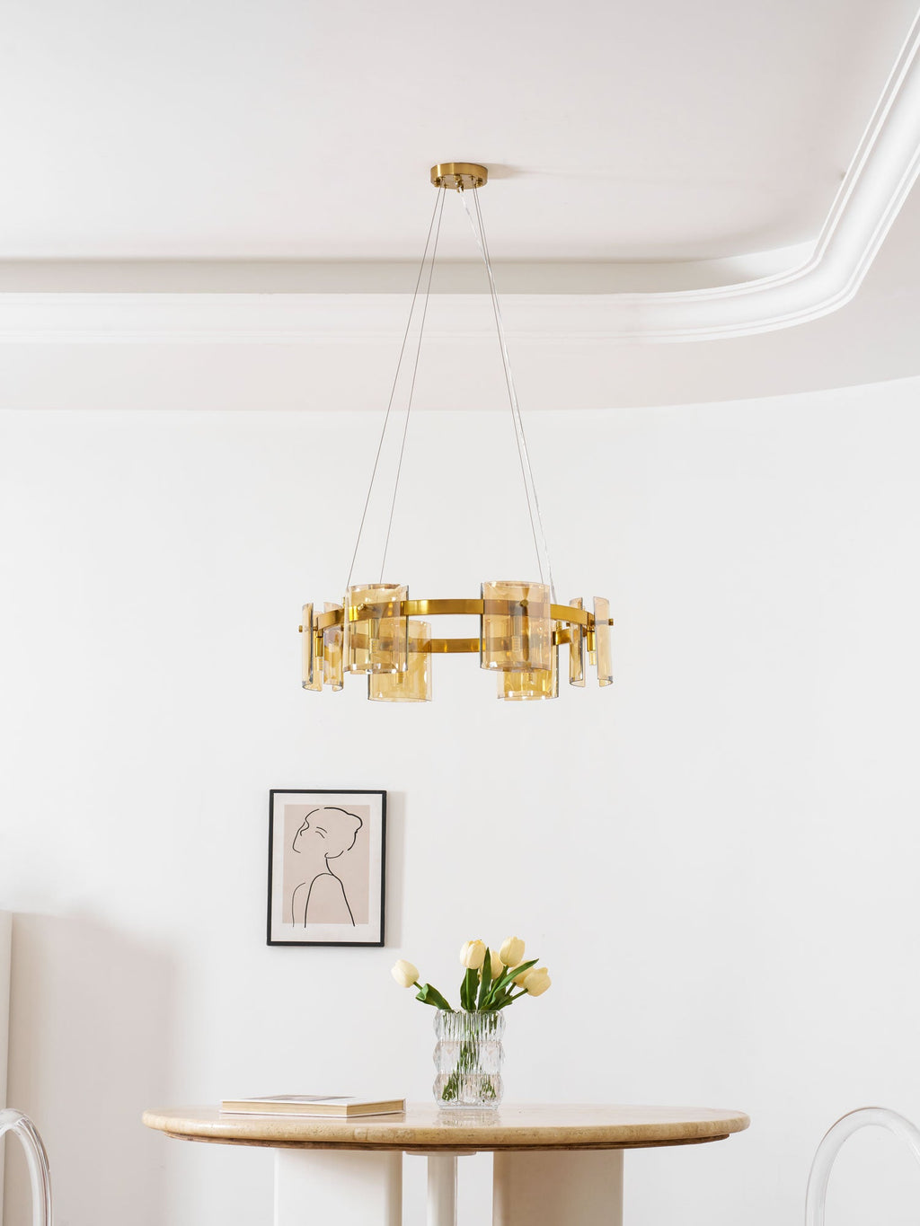 Gold-frame ring chandelier from Clérachic with amber glass, hung in a white room above a small round table and tulips.