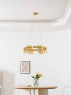 Gold-frame ring chandelier from Clérachic with amber glass, hung in a white room above a small round table and tulips.