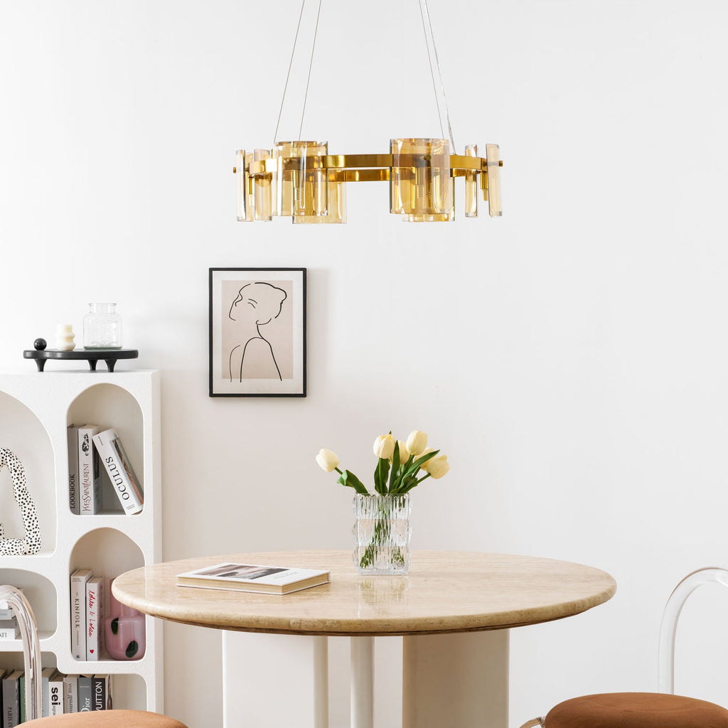 Close view of a gold-frame chandelier from Clérachic above a framed line portrait, a tulip vase and a round stone table.