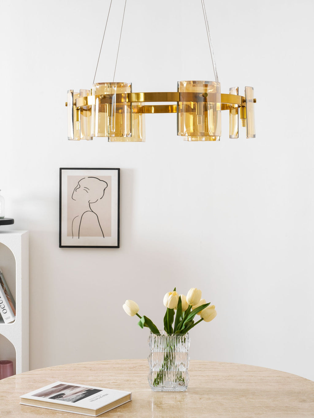 Gold-frame Clérachic chandelier with amber glass shades hung above a framed portrait, tulips in a glass vase and a design book.