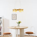 Gold-frame Clérachic chandelier with amber shades above a framed portrait, a vase of tulips and a round table with brown stools.
