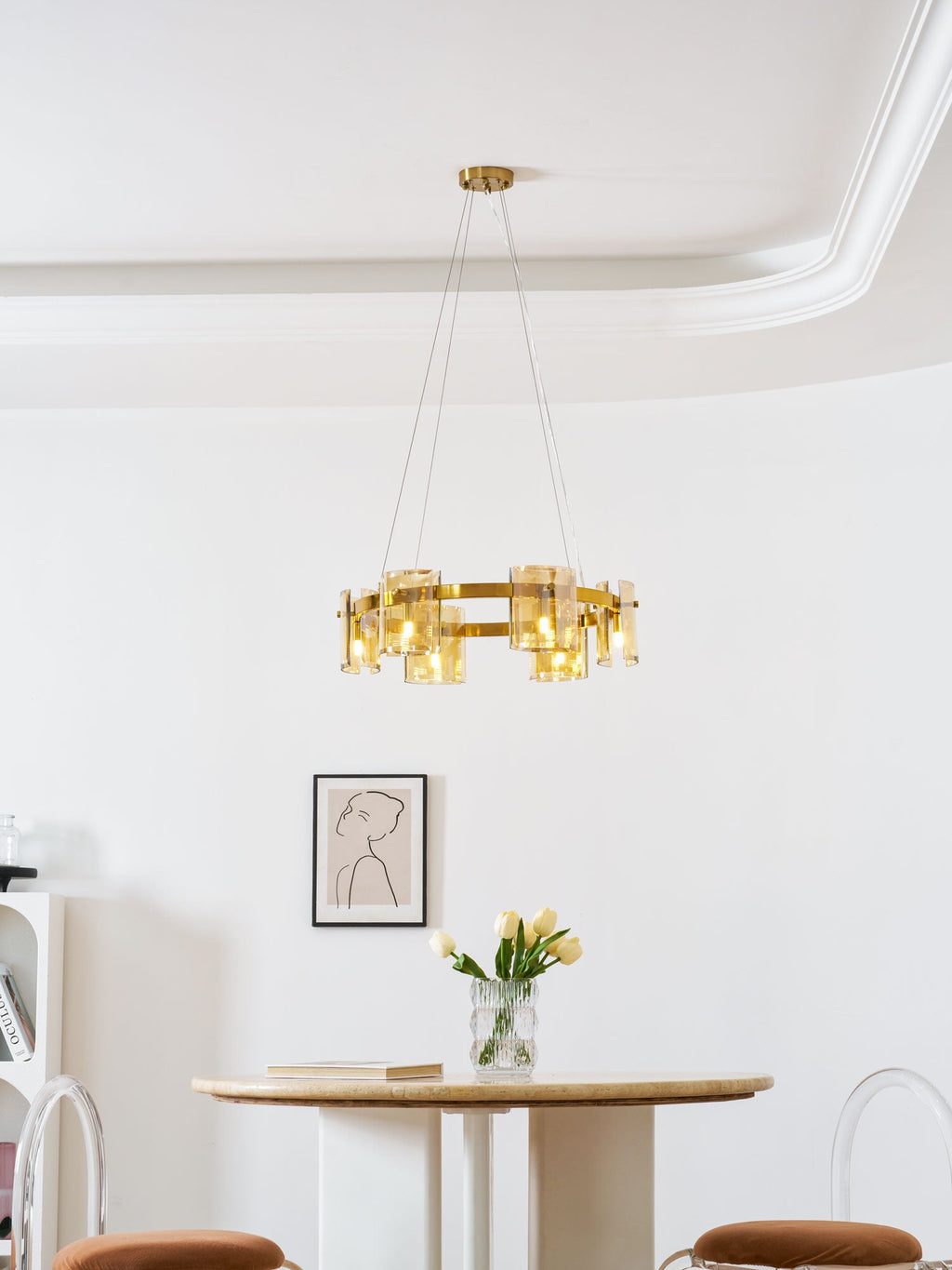 Lit gold-frame Clérachic chandelier with amber glass in a white room, with a framed portrait and a round table below.