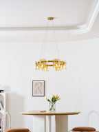 Lit gold-frame Clérachic chandelier with amber glass in a white room, with a framed portrait and a round table below.