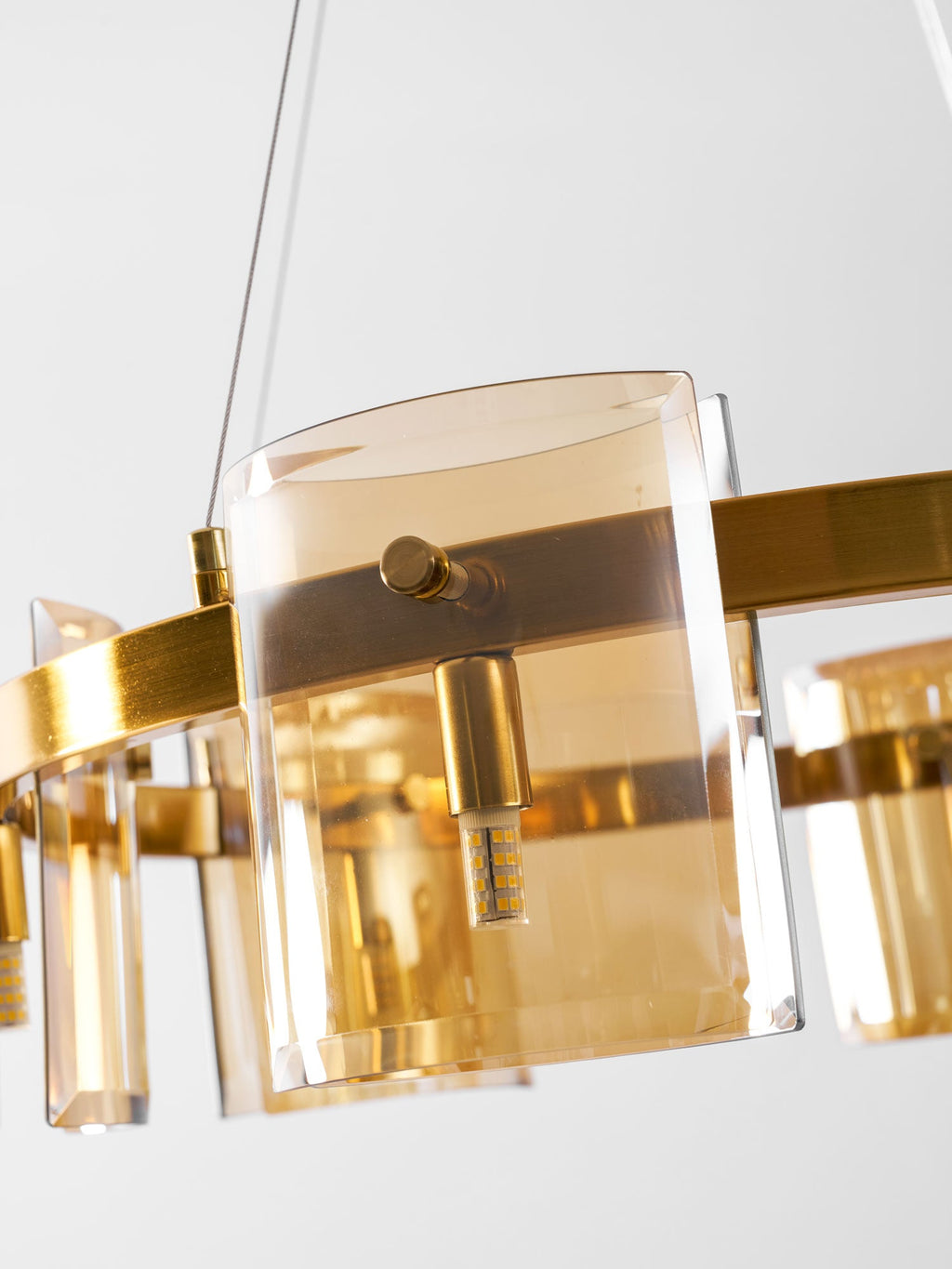 Close view of an amber glass shade, a brass-coloured pin and a small bulb on the gold band of this Clérachic chandelier.
