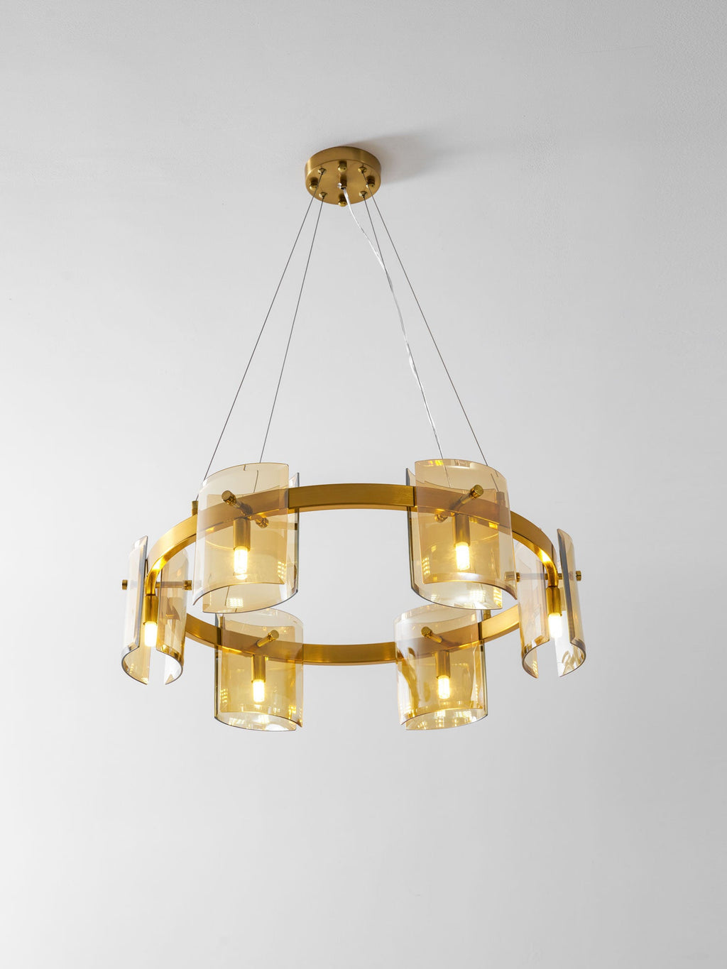 Lit gold-frame ring chandelier from Clérachic with six amber glass shades and a round gold canopy, on a pale grey backdrop.