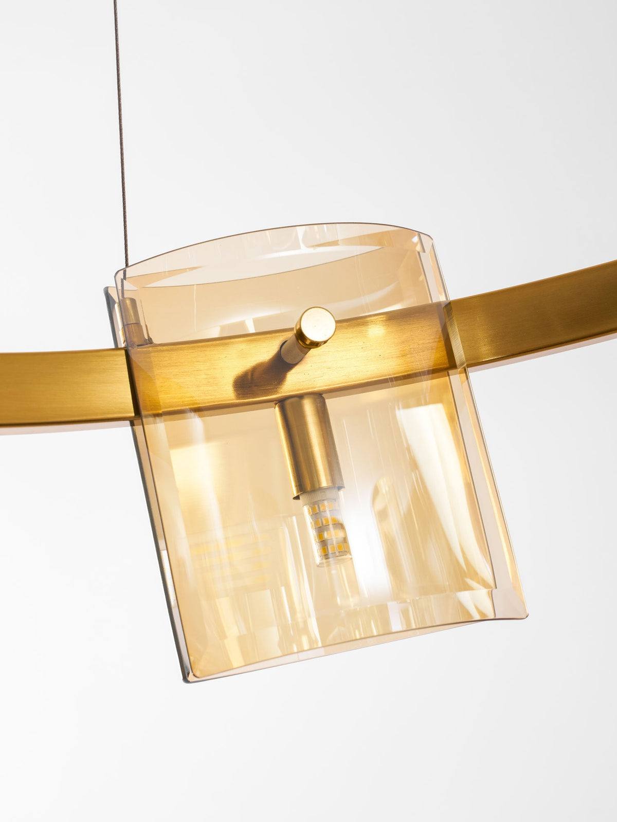Close view of one amber glass shade on this Clérachic chandelier, with the gold band and a bulb glowing inside.
