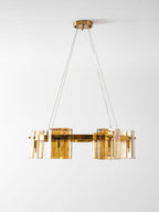 Side view of a gold-frame Clérachic chandelier with amber glass panels and a gold canopy, hung low on a pale backdrop.