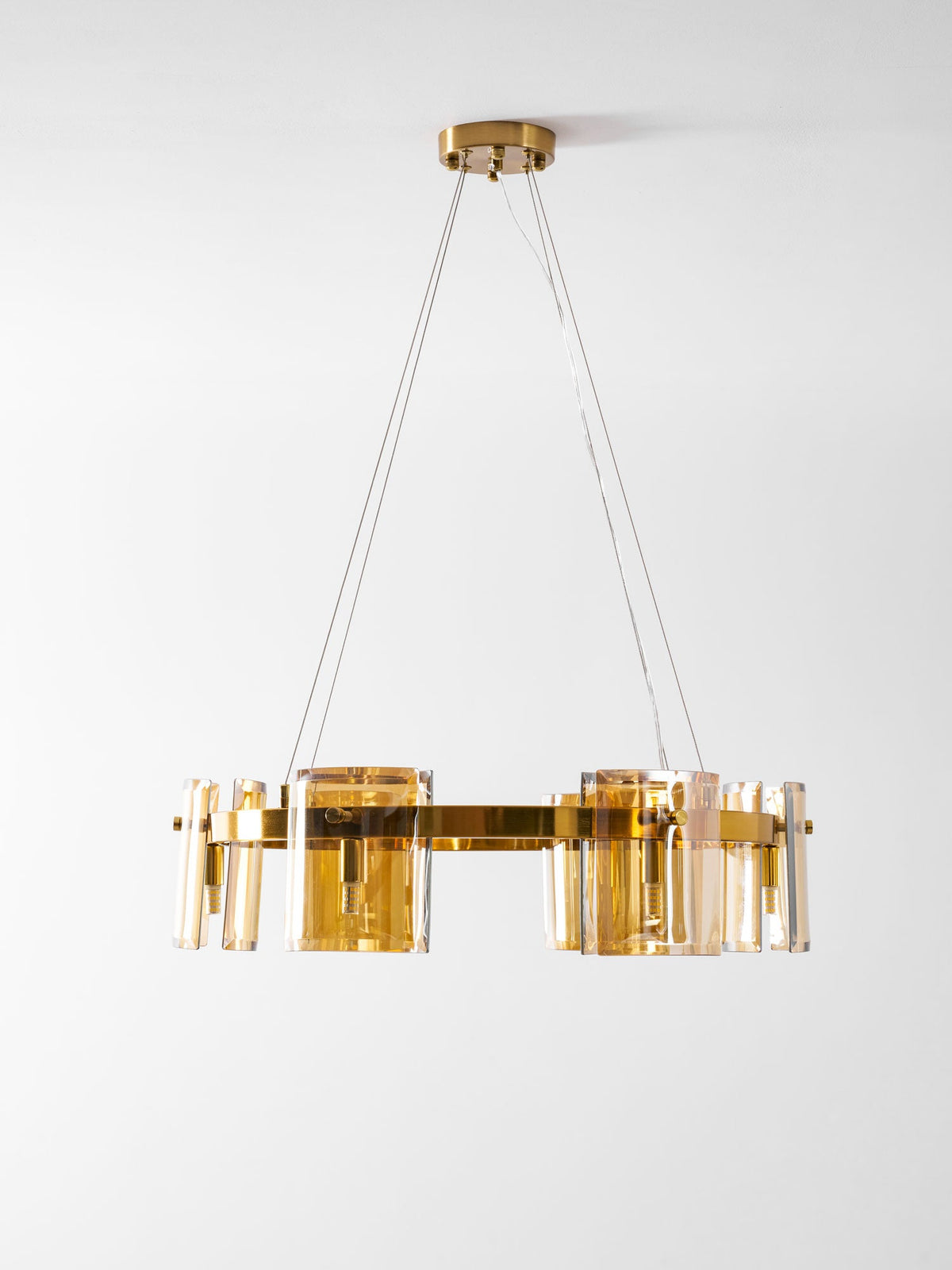 Side view of a gold-frame Clérachic chandelier with amber glass panels and a gold canopy, hung low on a pale backdrop.