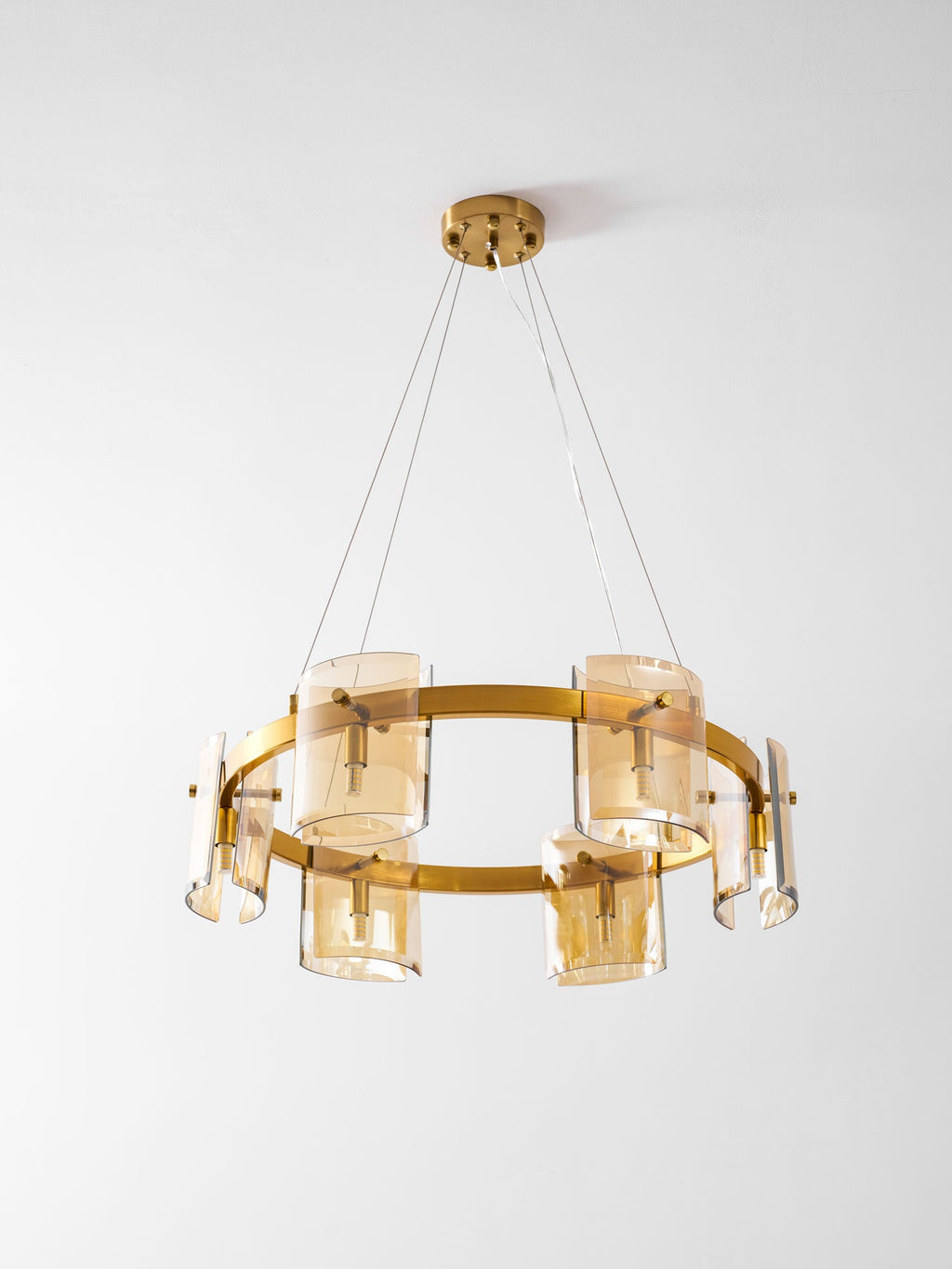 Gold-frame Clérachic chandelier with six amber glass shades and a round gold canopy, seen from slightly below on a pale grey backdrop.