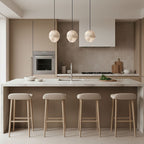 Three Clérachic Lunar pendants in a row above a pale kitchen island with oak stools.