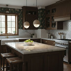 Two Clérachic Lunar pendants over a dark kitchen island with floral wallpaper behind.