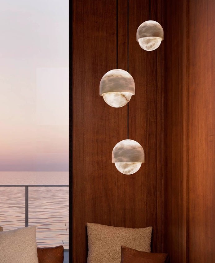 Three Clérachic Lunar pendants staggered against timber panelling with a sea view beyond.