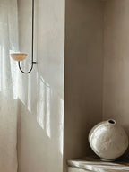 The Clérachic Lunaris single light on plaster beside a linen curtain and a stone vase.