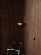 Clérachic Lunaris single-arm light on a dark timber wall in a dim, quiet room.