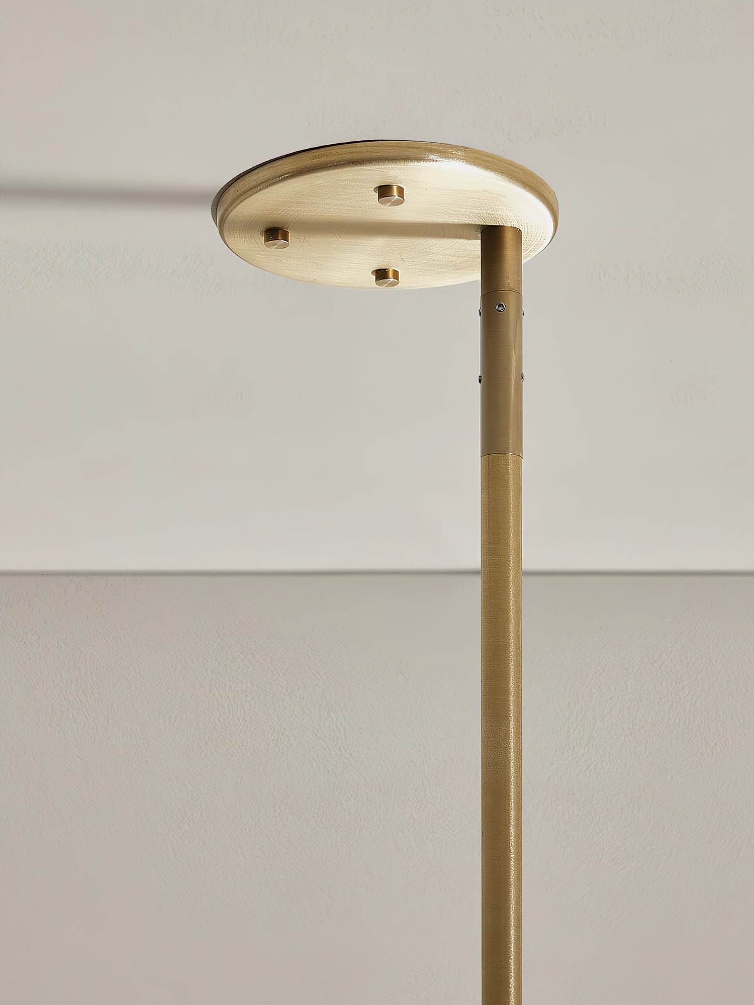 Detail of the Clérachic Lunaris ceiling plate in brass against a pale ceiling.